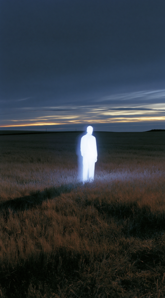 Glowing human figure standing in a field at twilight